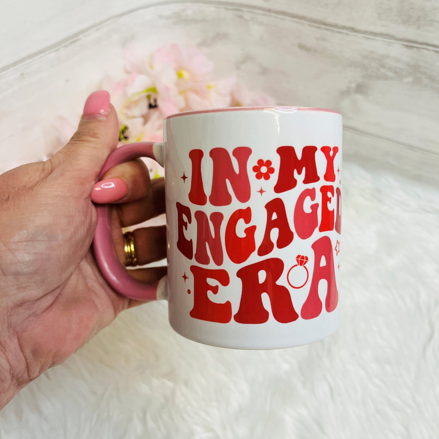 Hand holding a mug with 'IN MY ENGAGED ERA' text on a light background