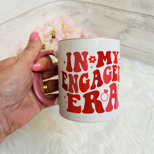 Hand holding a mug with 'IN MY ENGAGED ERA' text on a light background