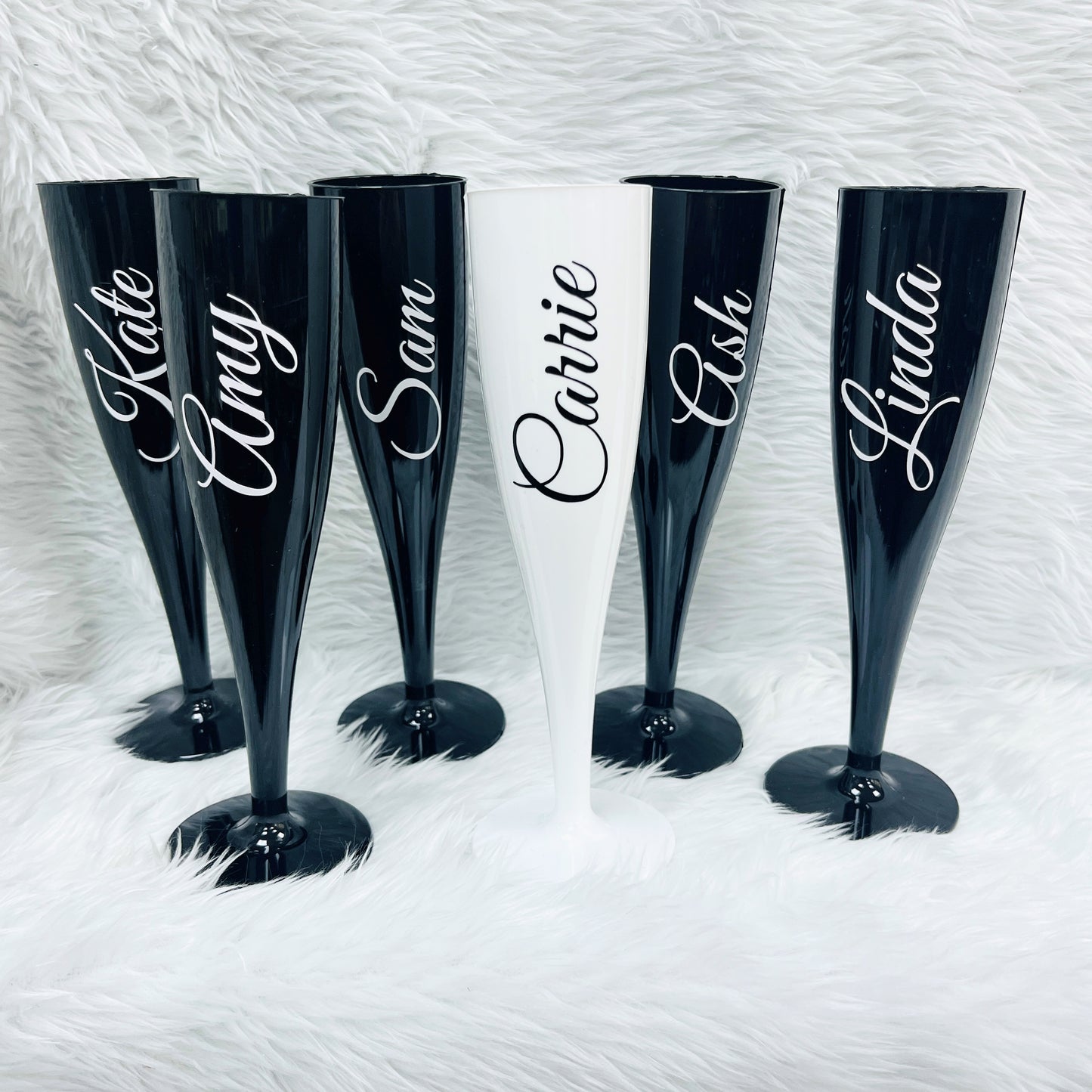 Set of personalised black and white champagne flutes with names on a textured white background
