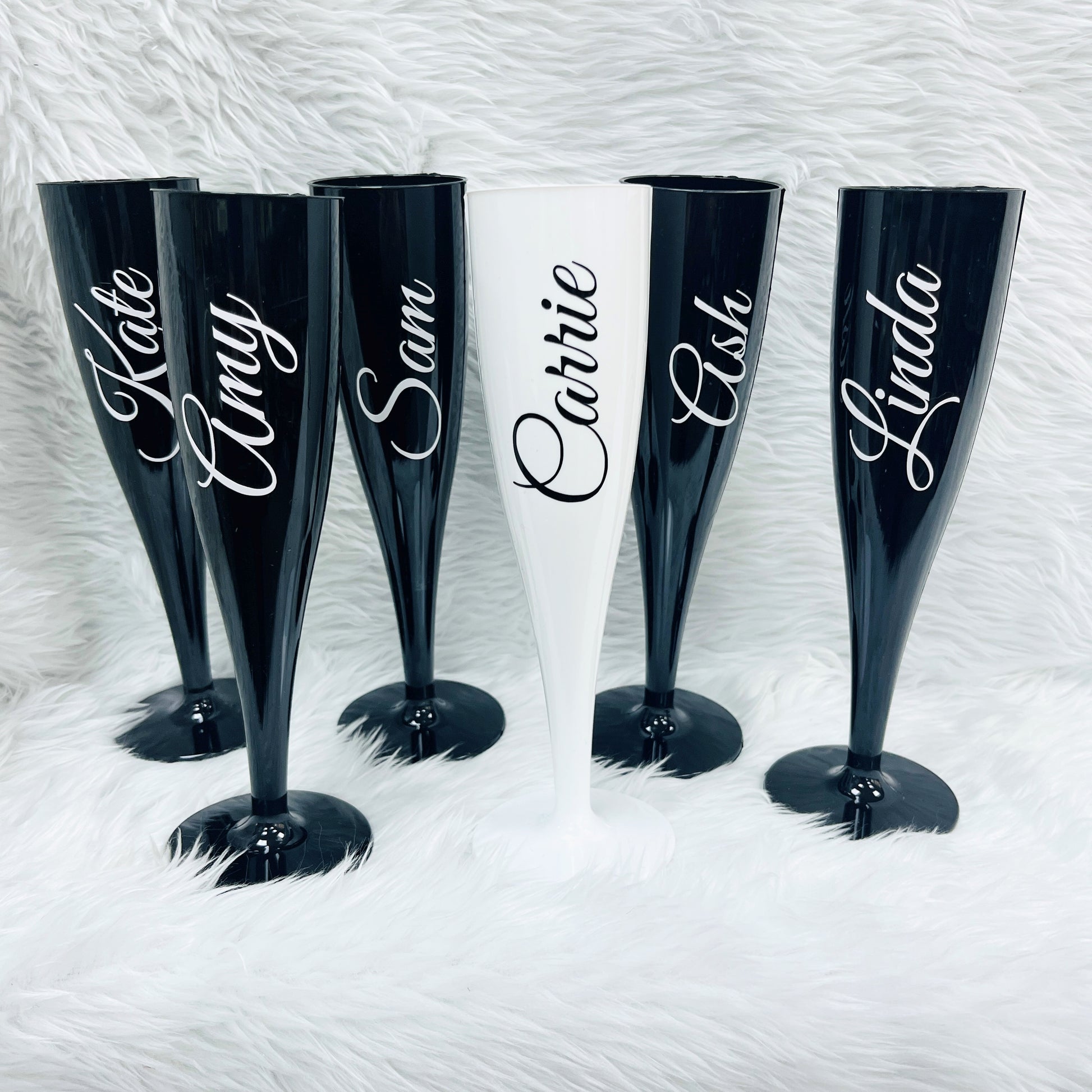 Set of personalised black and white champagne flutes with names on a textured white background