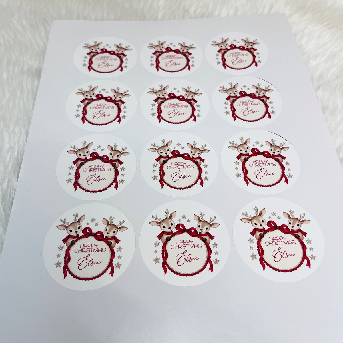 A sheet of round white Christmas stickers featuring red bows, reindeer, and the text 'Merry Christmas  Elsie' on a white background.