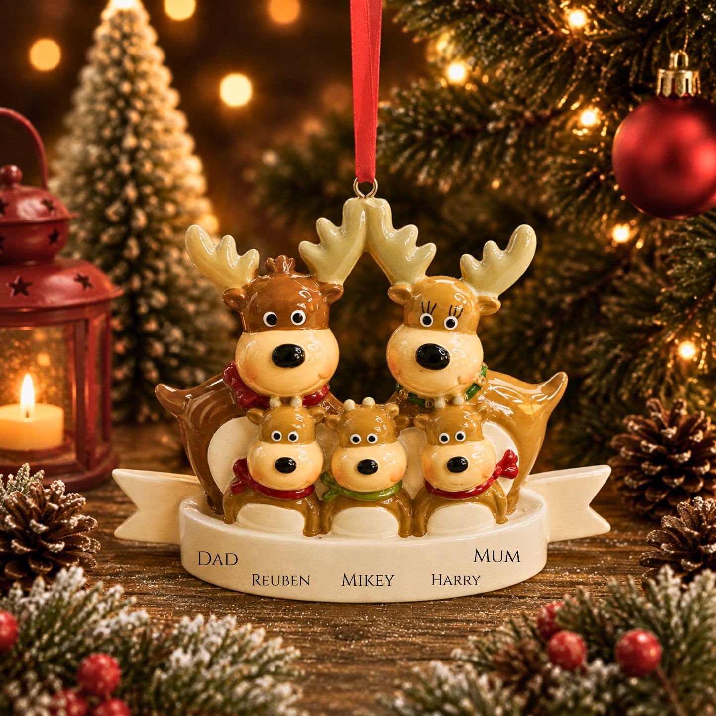 A Christmas ornament shaped like a family of five reindeer , displayed on a rustic wooden surface with a blurred Christmas tree, lantern, and pinecones in the background.