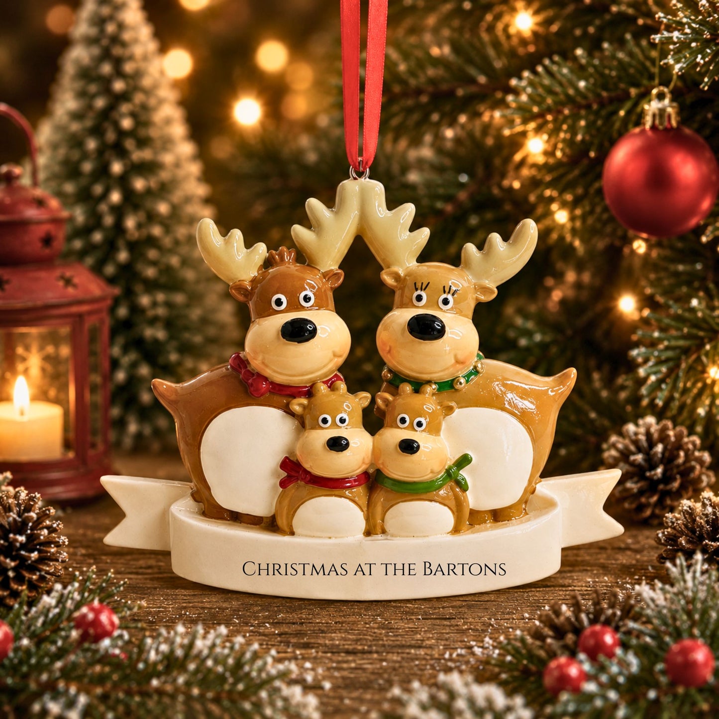 A ceramic Christmas ornament featuring a family of four reindeer with the text 'CHRISTMAS AT THE BARTONS' on a banner base, hanging from a red ribbon against a festive Christmas tree background.