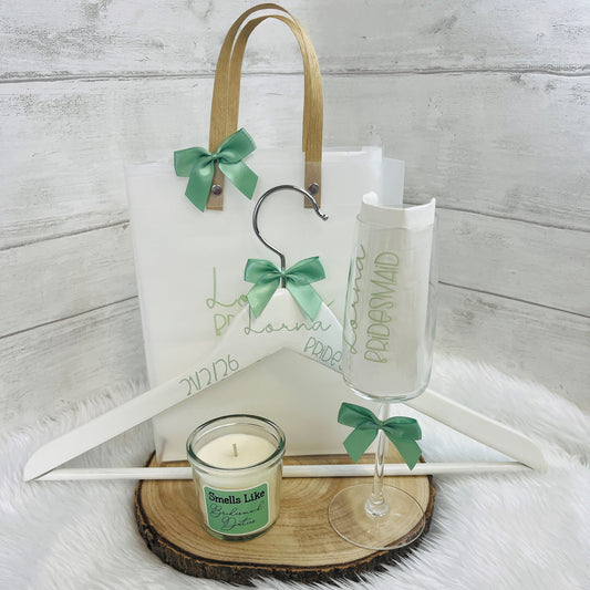 Set of wedding accessories including a candle, glass, Wooden Hanger and gift bag with green ribbons on a wooden surface.