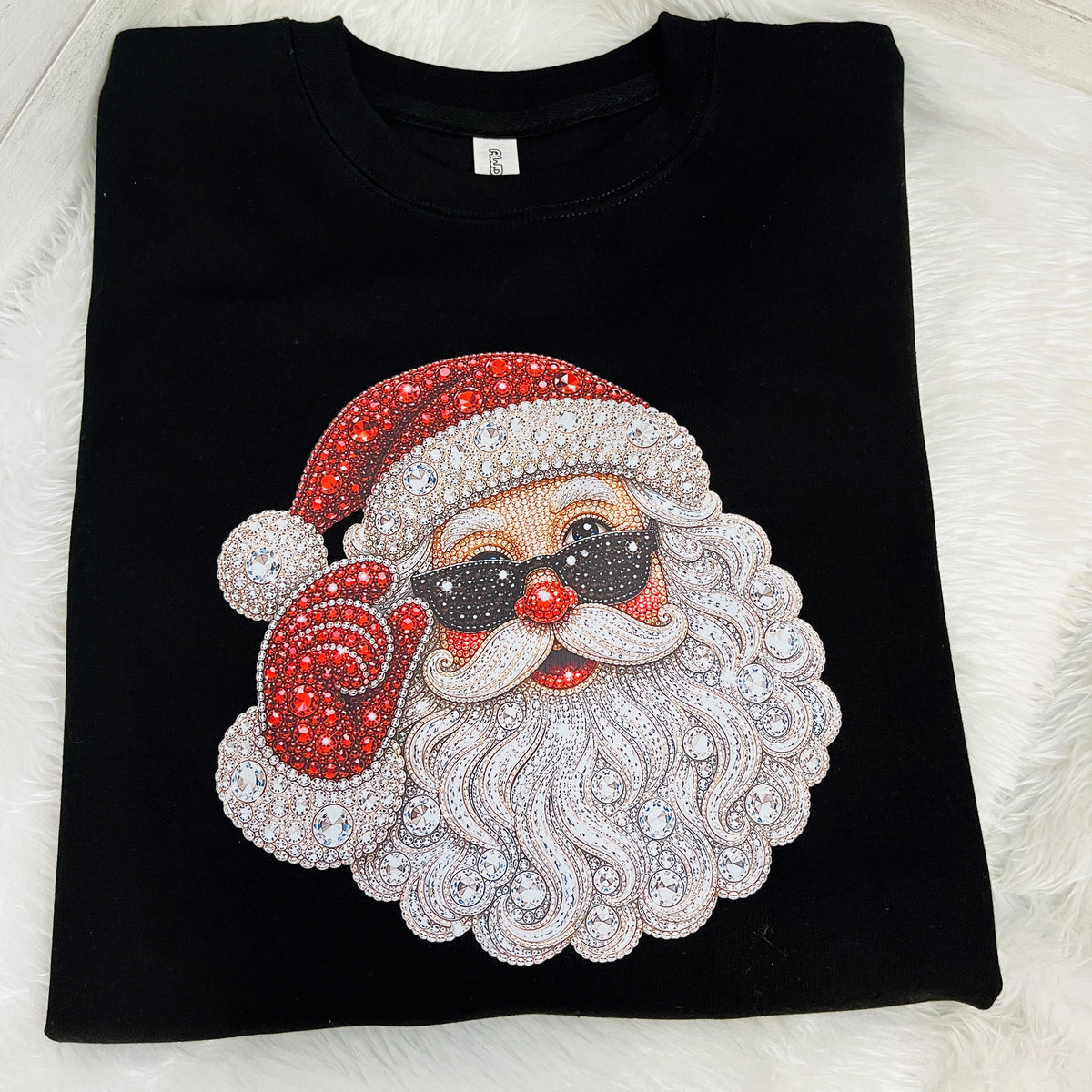 A black crewneck sweatshirt laid flat on a white faux fur surface, featuring a large rhinestone-decorated Santa Claus face graphic on the front.