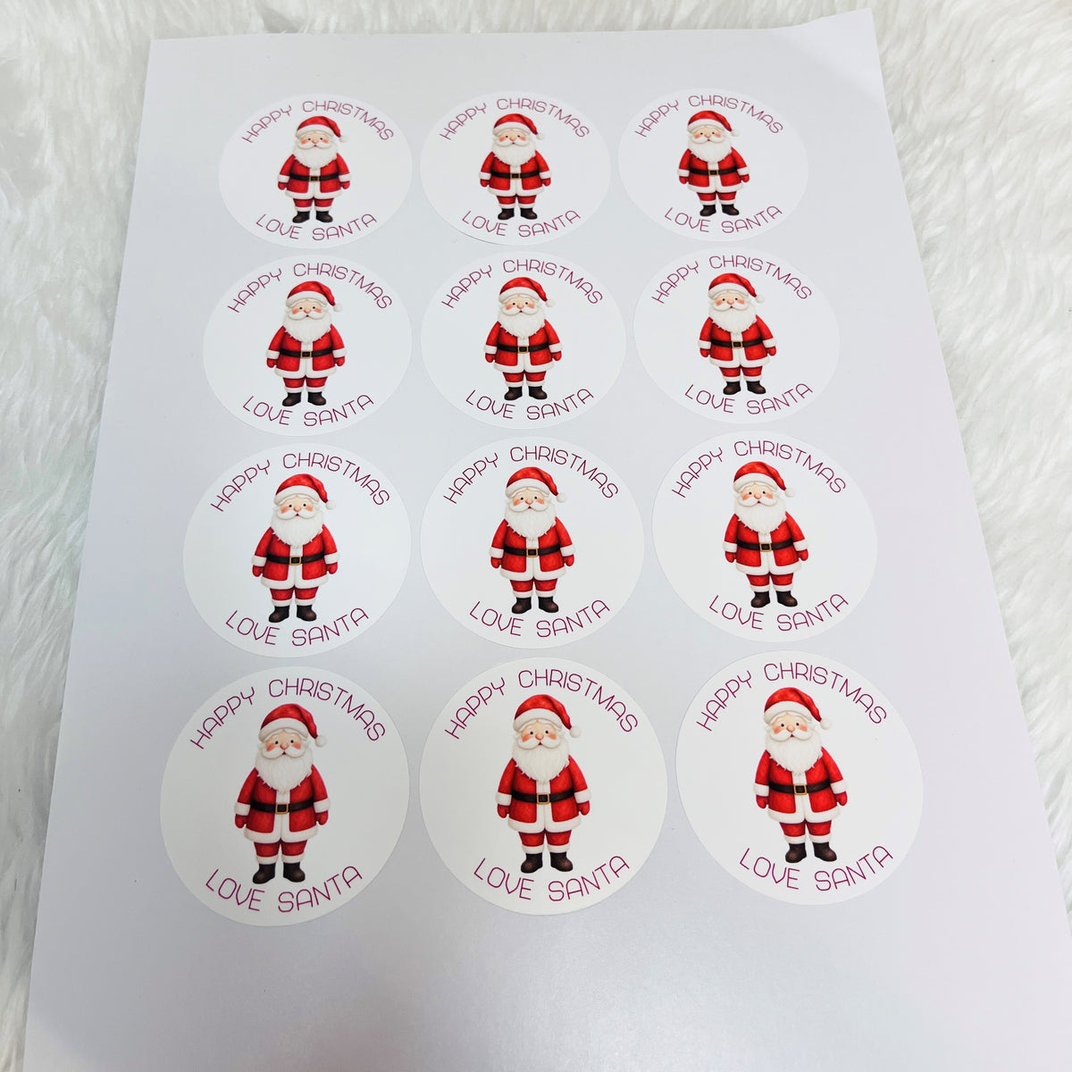 A sheet of round white stickers featuring a cartoon Santa Claus and the text 'HAPPY CHRISTMAS LOVE SANTA' repeated in three columns of four.