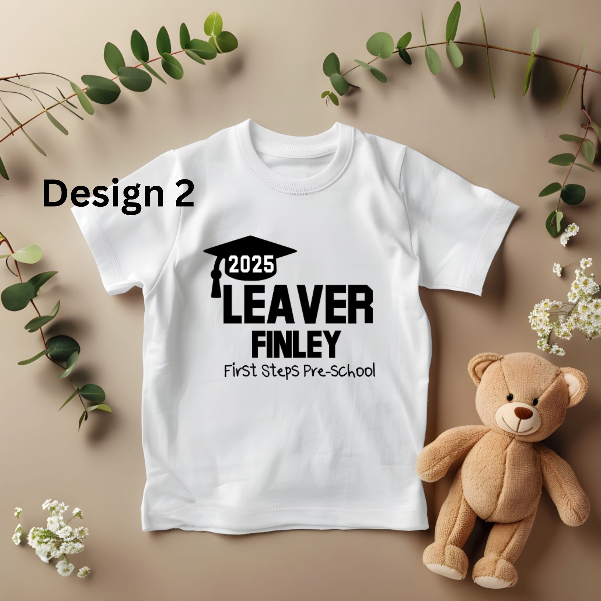 White t-shirt with '2025 Leaver Finley First Steps Pre-School' design on a beige background with a teddy bear and greenery.