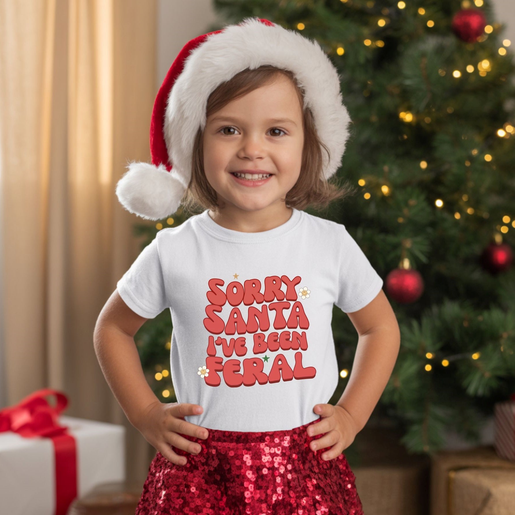 a small child wearing a santa hat and a white T-shirt with the text 'sorry santa I've been feral' on the front