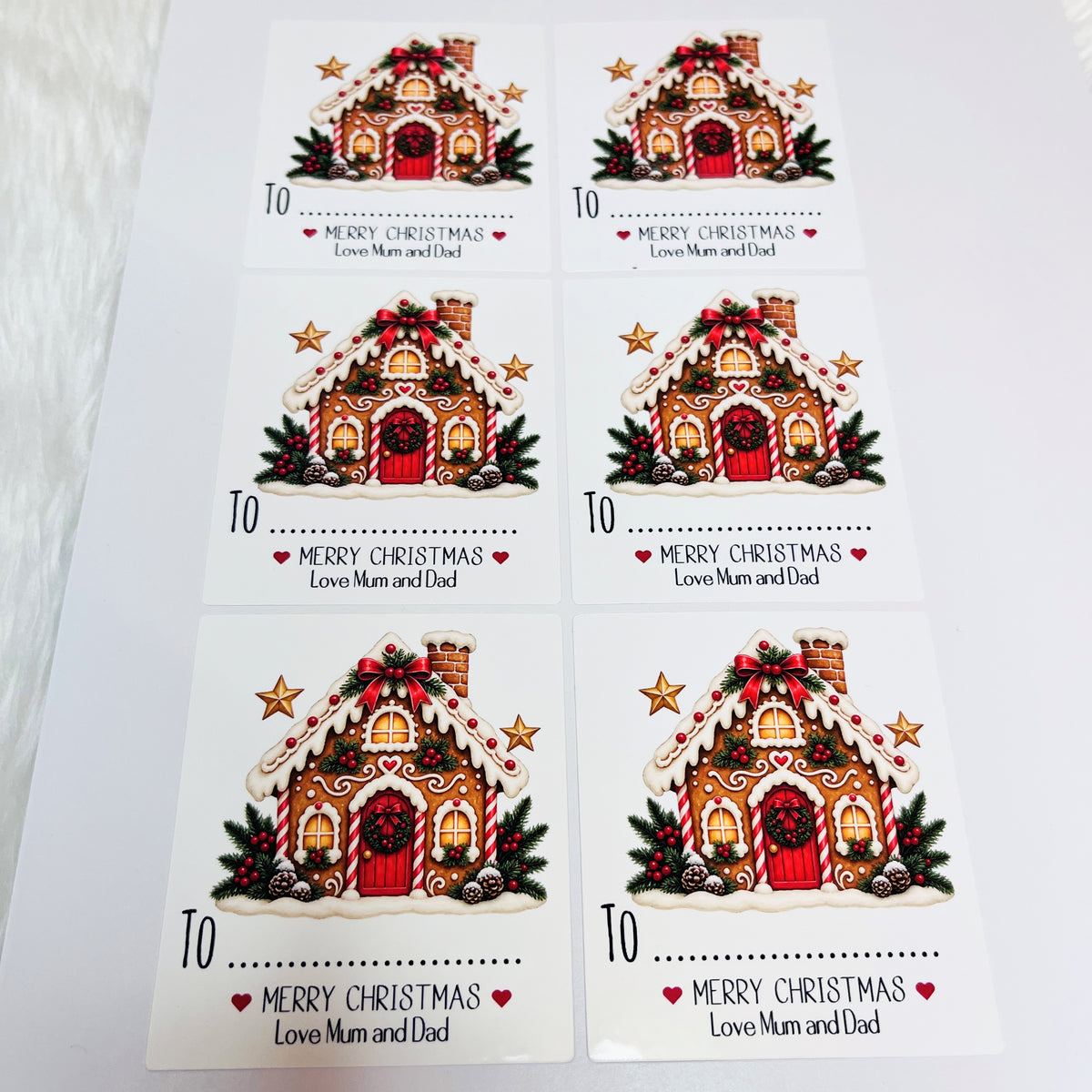 Six rectangular Gingerbread house stickers.  Each sheet shows an illustrated gingerbread house with red ornaments, green pine branches, stars, and the text 'MERRY CHRISTMAS Love Mum and Dad' 