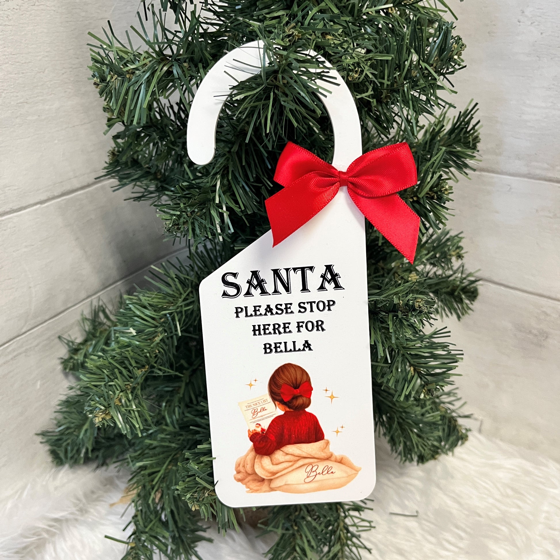Personalized Christmas decoration with a tag for Santa to stop, featuring a red bow and a child illustration.