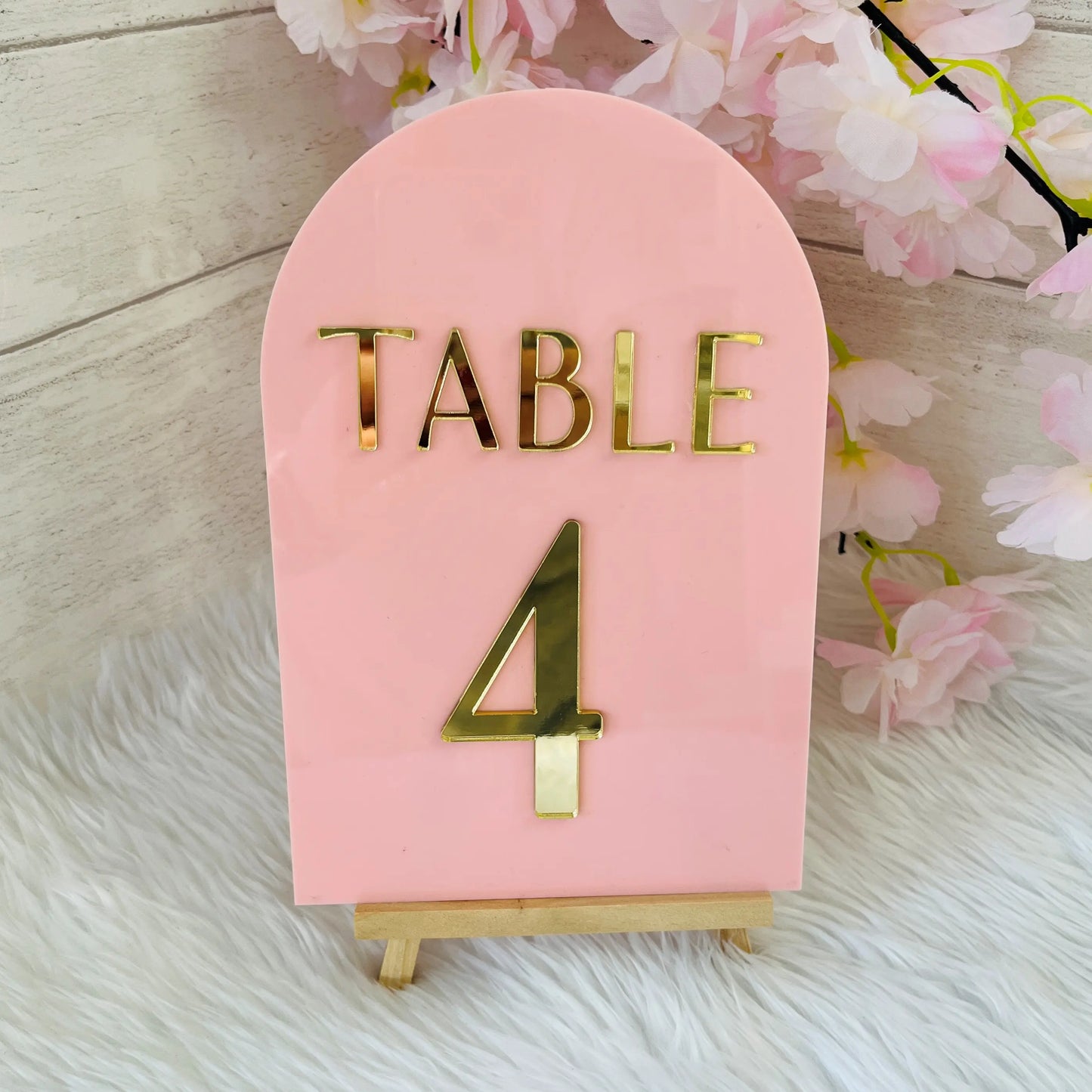 Pink table number with gold 'TABLE 4' on a wooden surface with floral decorations.
