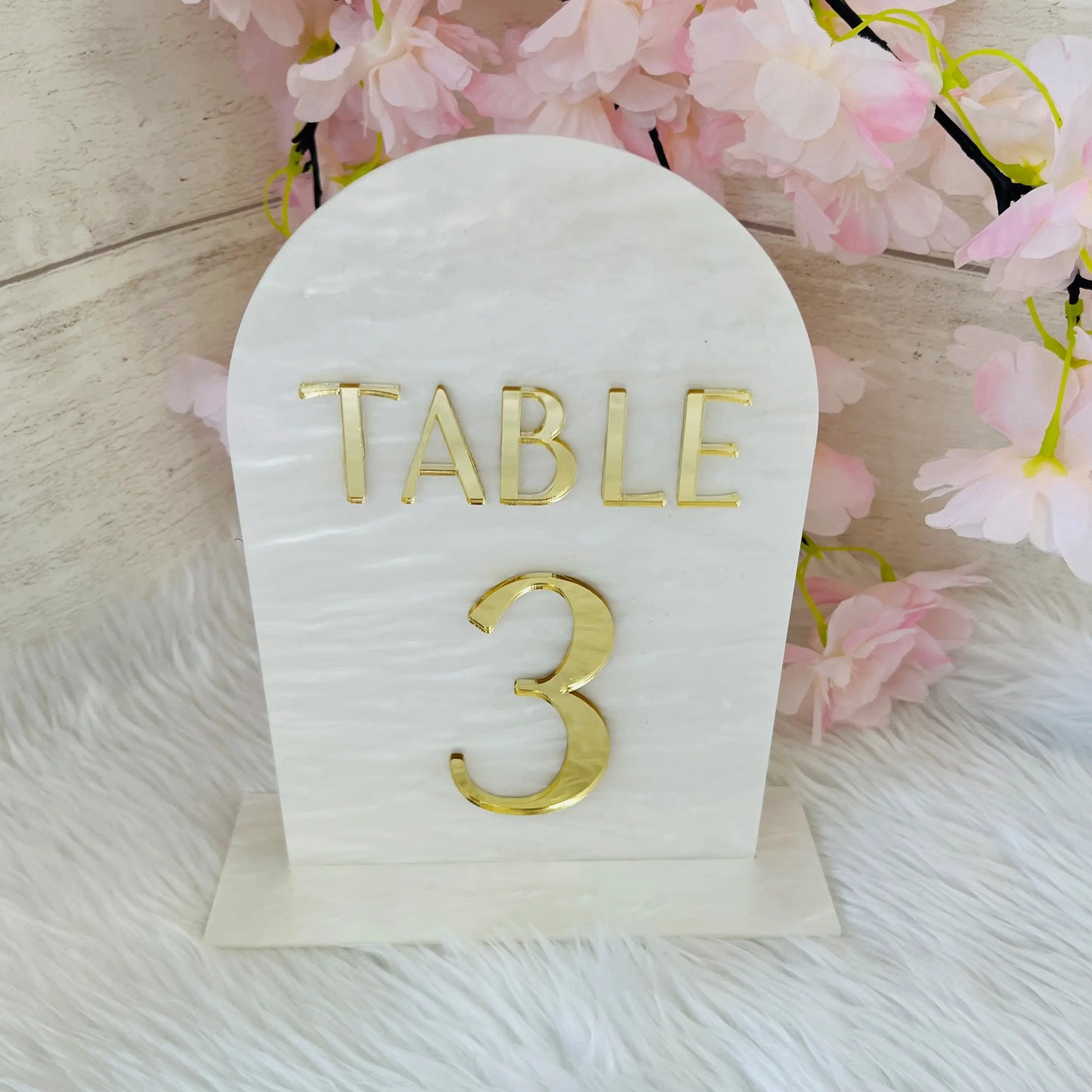 White swirl acrylic Table number with 'TABLE 3' in gold on a white background with pink flowers.
