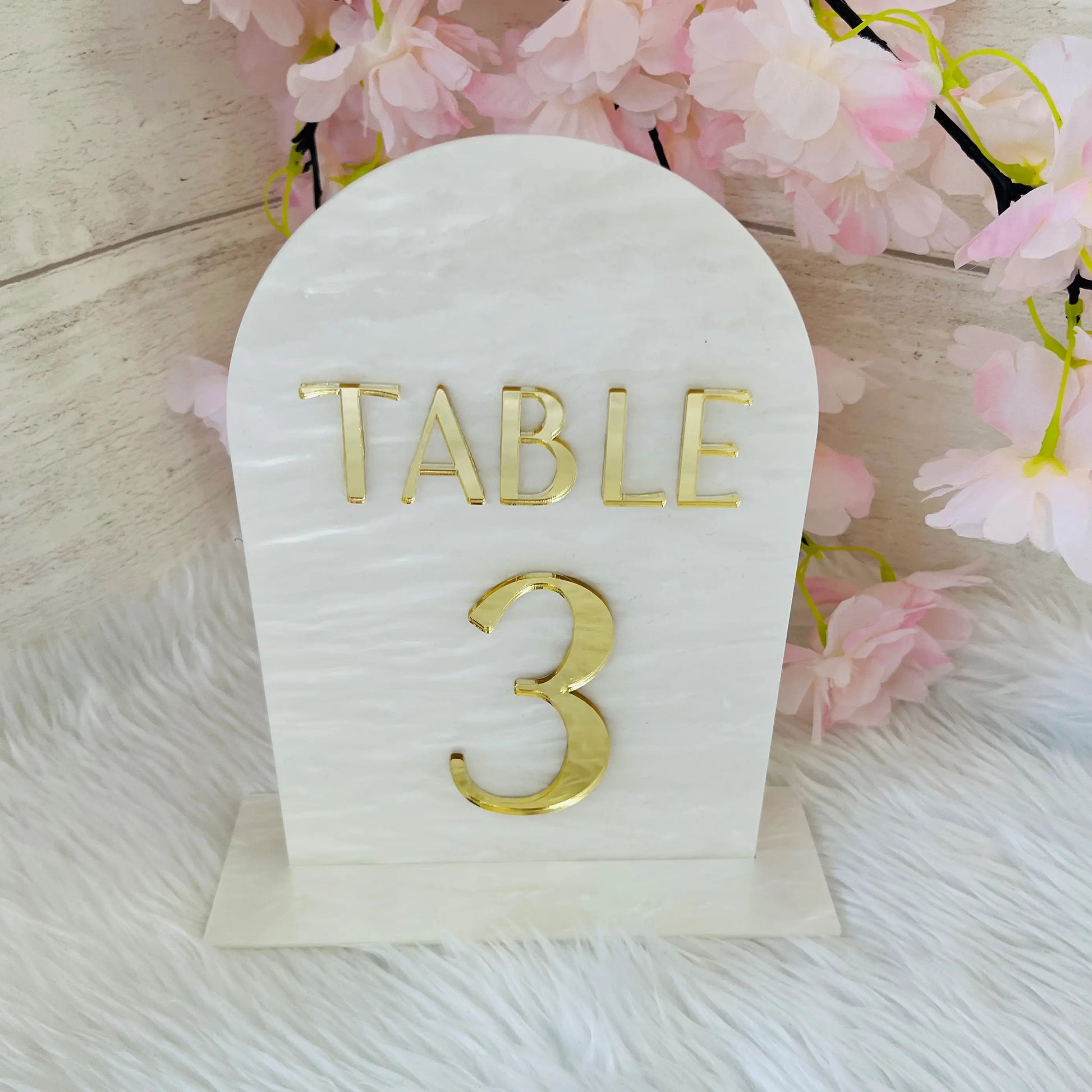 White swirl acrylic Table number with 'TABLE 3' in gold on a white background with pink flowers.