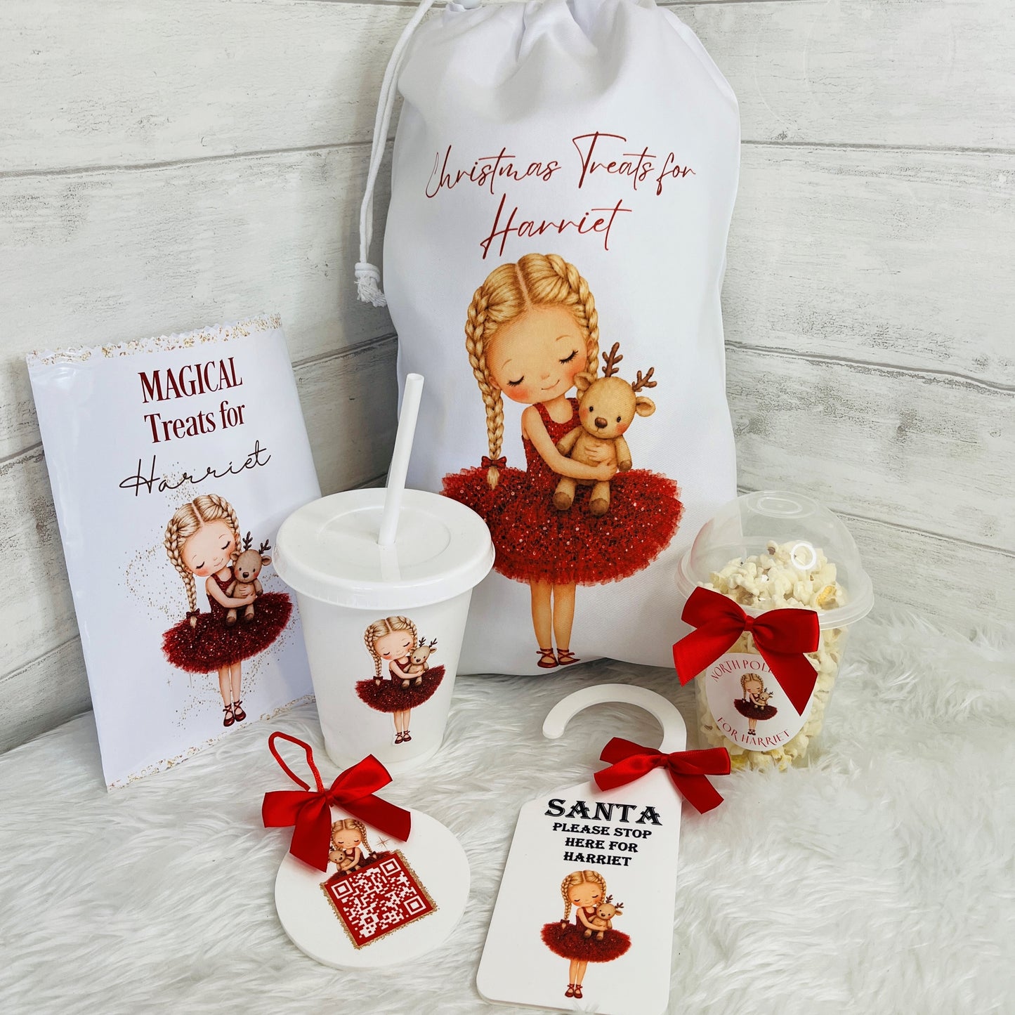 A personalised Christmas treats gift set for 'Harriet' featuring a white drawstring bag, a printed treat packet, a cup with a lid and straw, a snack pot, a 'Please Stop Here For Harriet' sign, and a santa tracker, all decorated with an illustration of a girl in a red tutu holding a reindeer.
