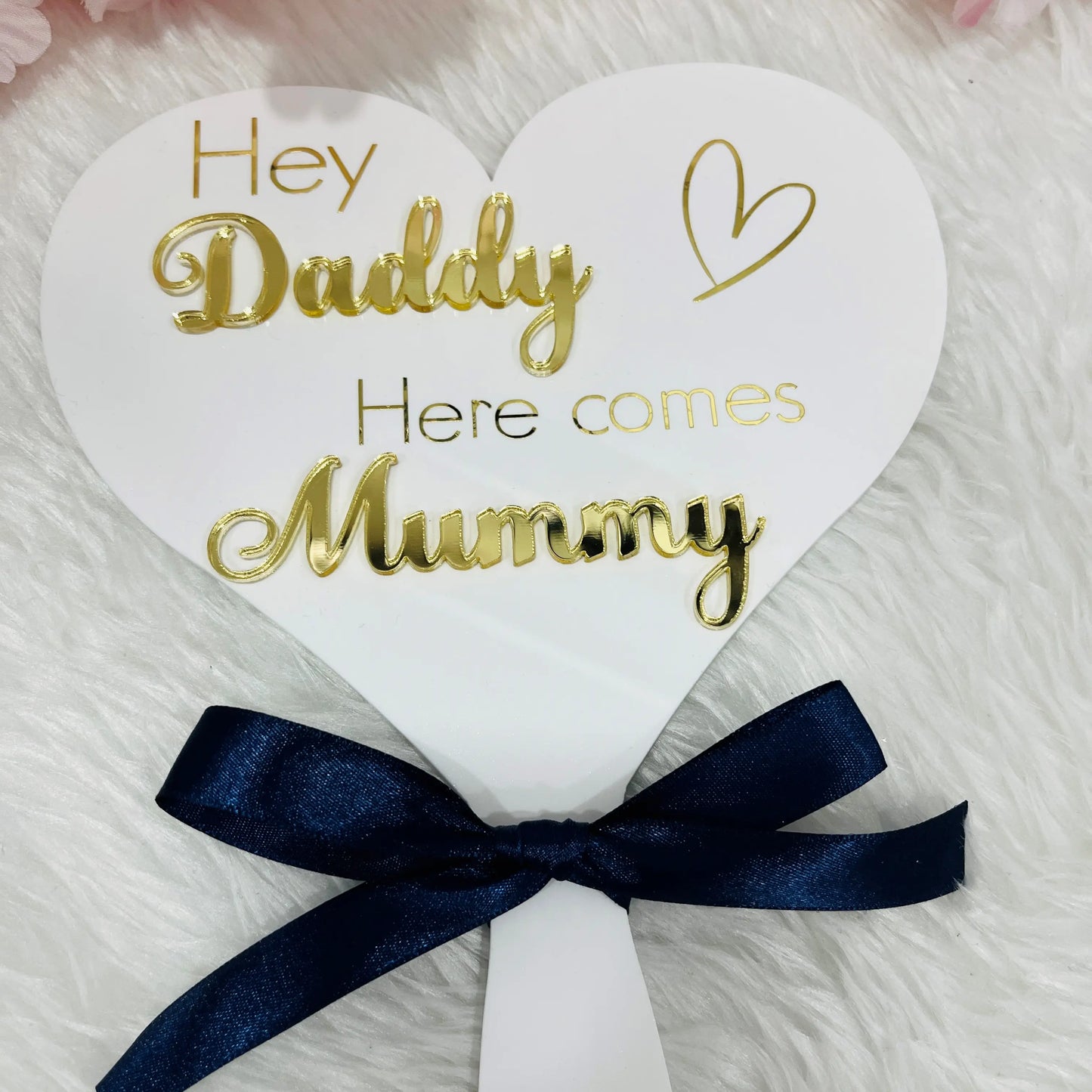 Heart-shaped sign with 'Hey Daddy Here comes Mummy' text and a navy ribbon on a white background