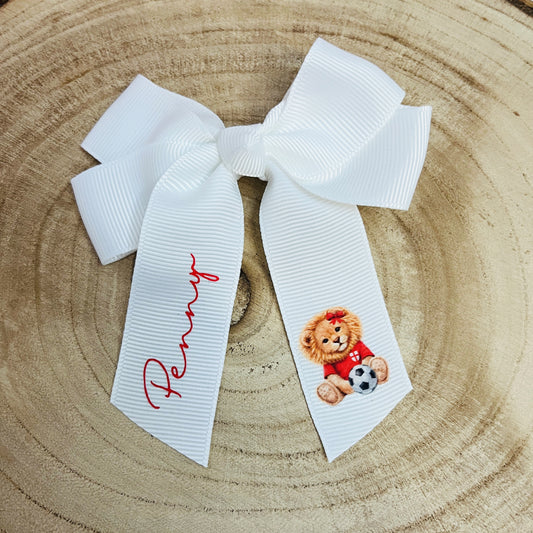 White 4inch grosgrain hair bow with a 'come on england' lion holding a football and the name 'Penny' on the other side on a wooden log slice background
